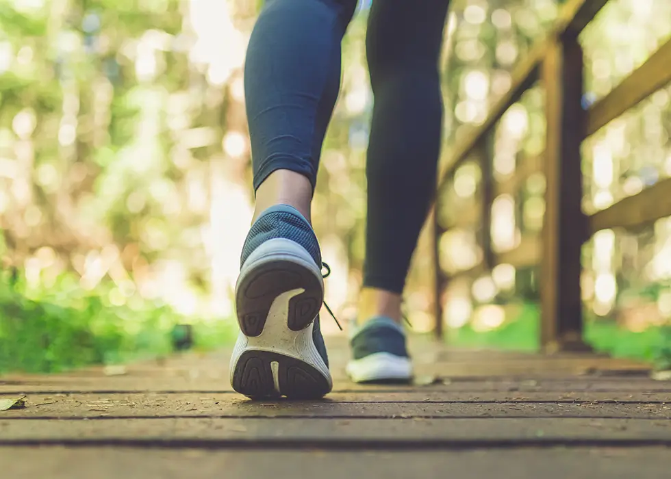 Frau joggt mit ihren Sportschuhen über eine Holzbrücke im Wald