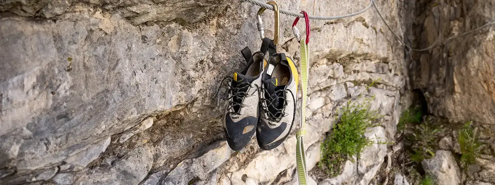 Kletterschuhe hängen an einem Kletterseil an einer Felswand